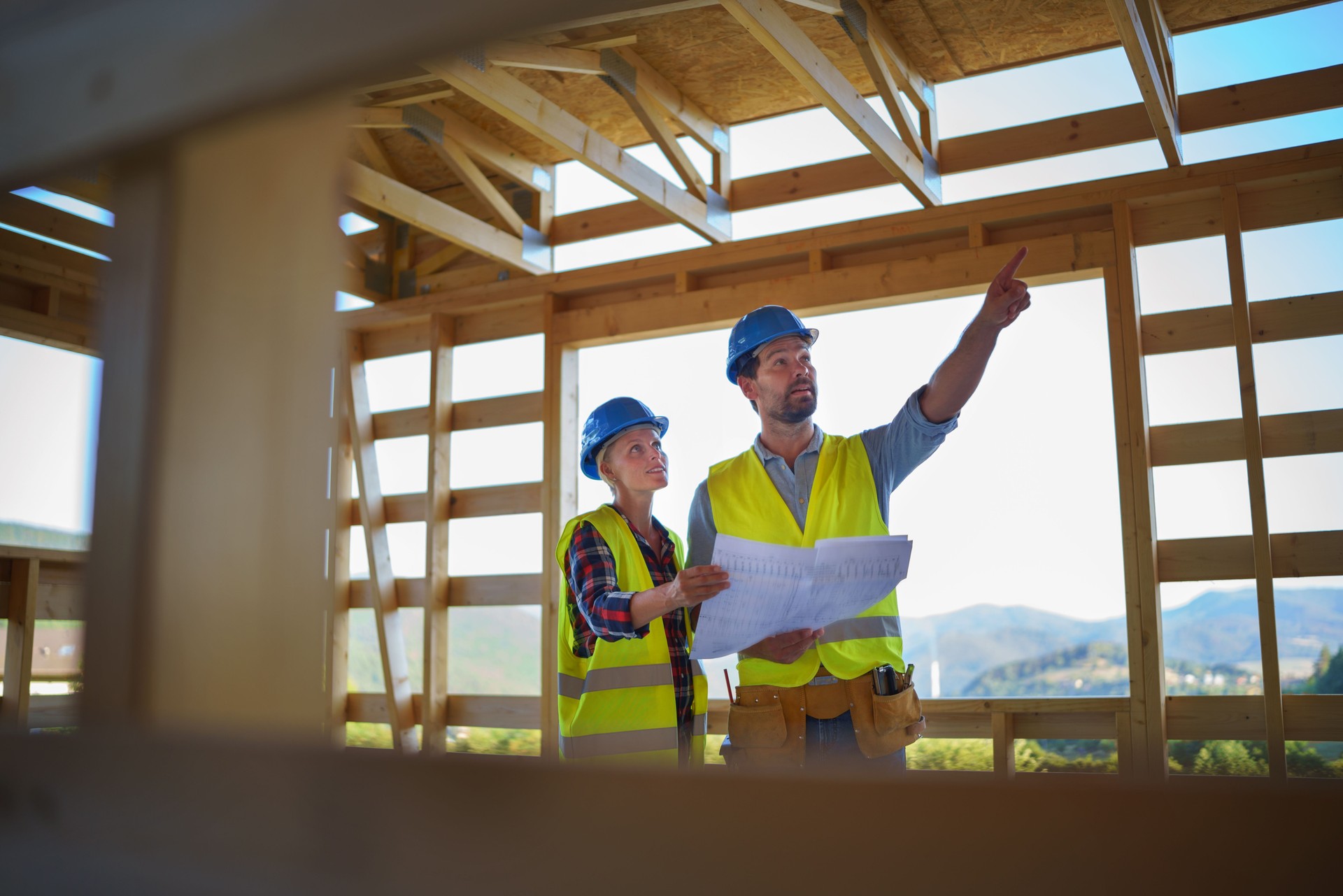 Construction engineers or architects with blueprints visiting and chcecking eco building site of wood frame house